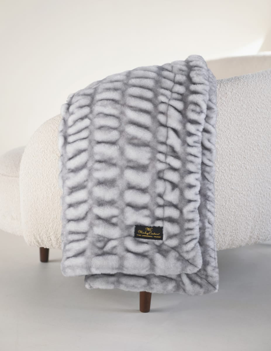 Hugs Moonbeam Blanket draped gracefully over a soft sofa, featuring a cozy gray design and textured surface.