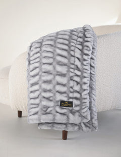Hugs Moonbeam Blanket draped gracefully over a soft sofa, featuring a cozy gray design and textured surface.