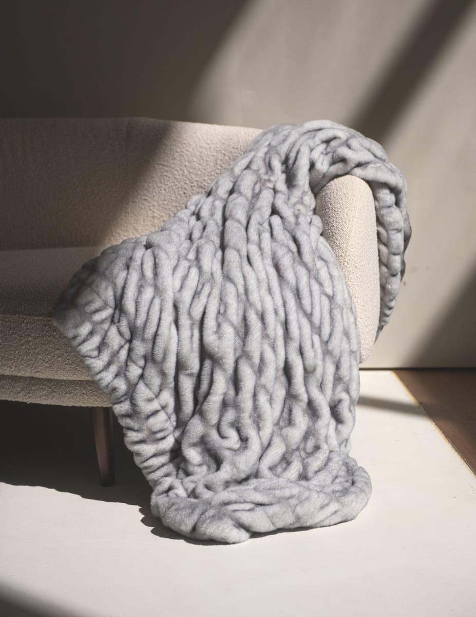Hugs Moonbeam Blanket laid over a cozy chair, showcasing its plush, two-toned gray design and modern style.