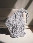 Hugs Moonbeam Blanket laid over a cozy chair, showcasing its plush, two-toned gray design and modern style.