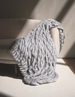 Hugs Moonbeam Blanket laid over a cozy chair, showcasing its plush, two-toned gray design and modern style.
