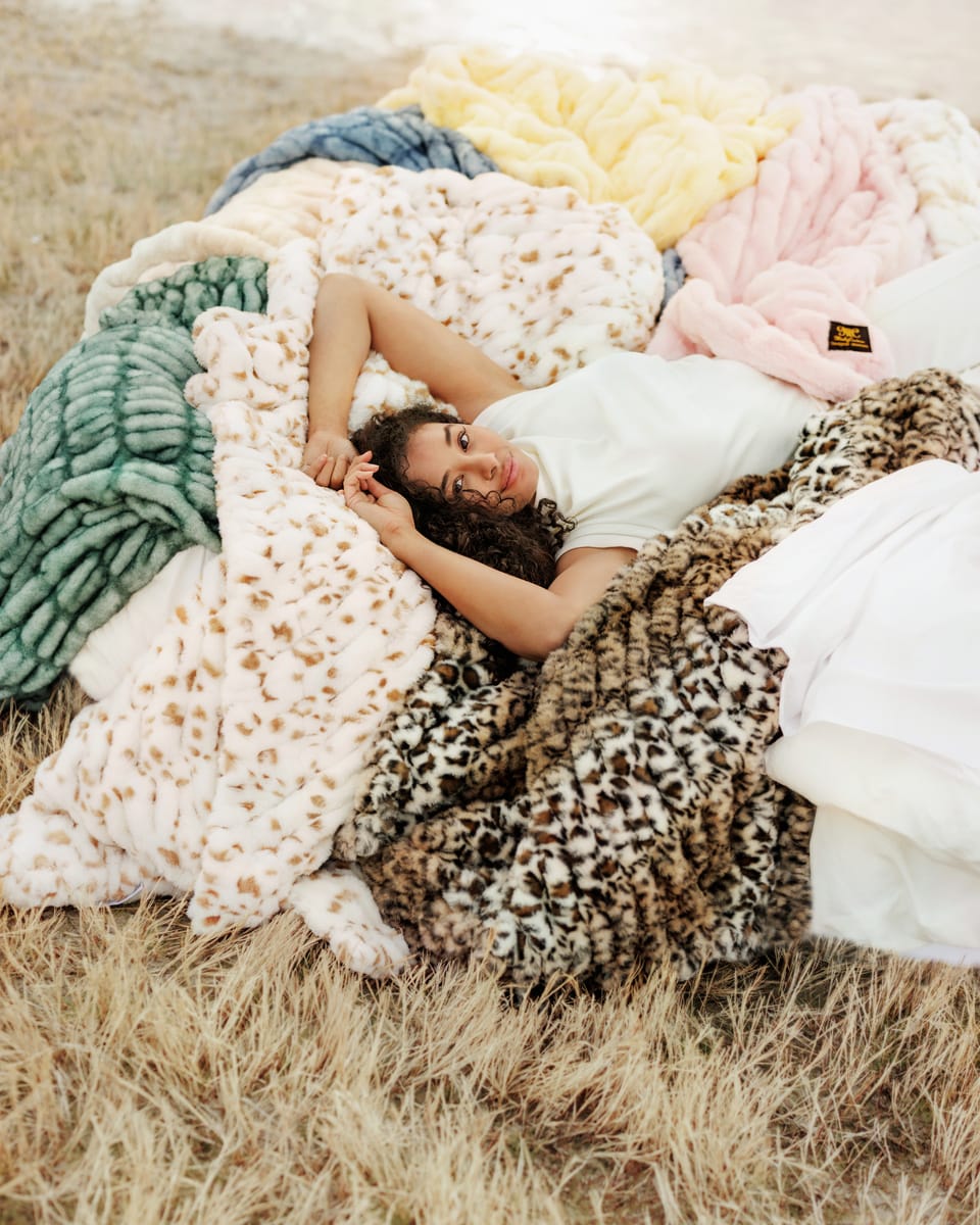 Woman lying on a blanket with blankets of various textures and colors in a natural setting.