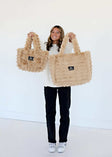 A woman showcasing two sizes of the Annie Bag Ripple Ecru, a luxurious and stylish accessory.