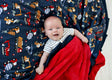 Baby smiling on a Construction Zone Blanket featuring construction vehicles on a navy background with red plush backing.