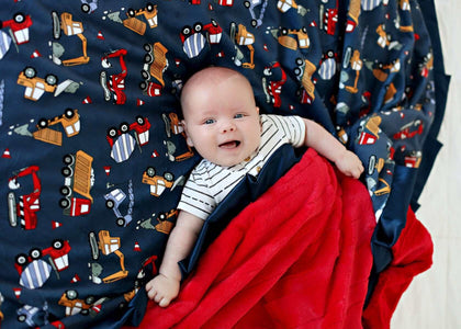 Baby smiling on a Construction Zone Blanket featuring construction vehicles on a navy background with red plush backing.