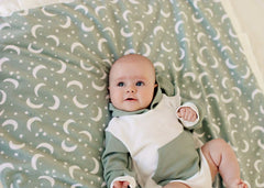 Baby lying on the Twilight Sky Blanket with cream stars and crescent moons on a sage green background.