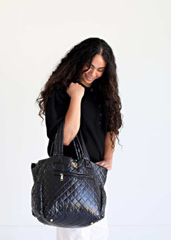 Woman smiling while holding the Patent Leather Black Everything Bag, showcasing its stylish quilted design.
