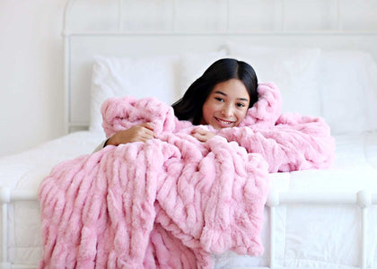 A girl wrapped in a cozy Hugs Cookie Pink Blanket, showcasing its plush texture and comfort on a bed.