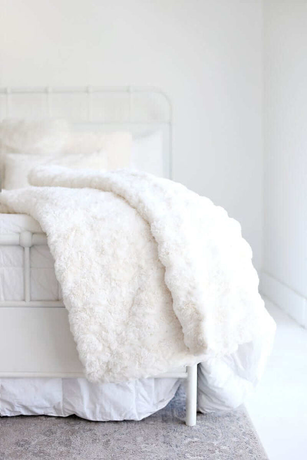 Ultra Sorbet Marshmallow Cream Blanket draped over a white bed, showcasing its luxurious faux fur texture.