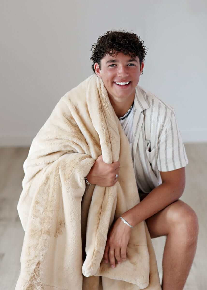 Lush True Caramel Blanket held by a smiling young man, showcasing its plush texture and cozy design.