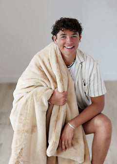 Lush True Caramel Blanket held by a smiling young man, showcasing its plush texture and cozy design.