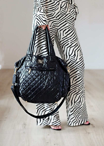 Everything Bag Patent Leather Black held by a model in stylish zebra print pants.