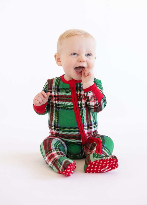 Baby wearing a green plaid Infant Unisex Zipper Footie sleeper with red zipper, sitting on a white background.