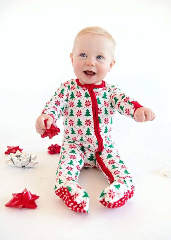 Infant Unisex Zipper Footie with Poinsettia and Tree worn by a baby, surrounded by festive decorations.