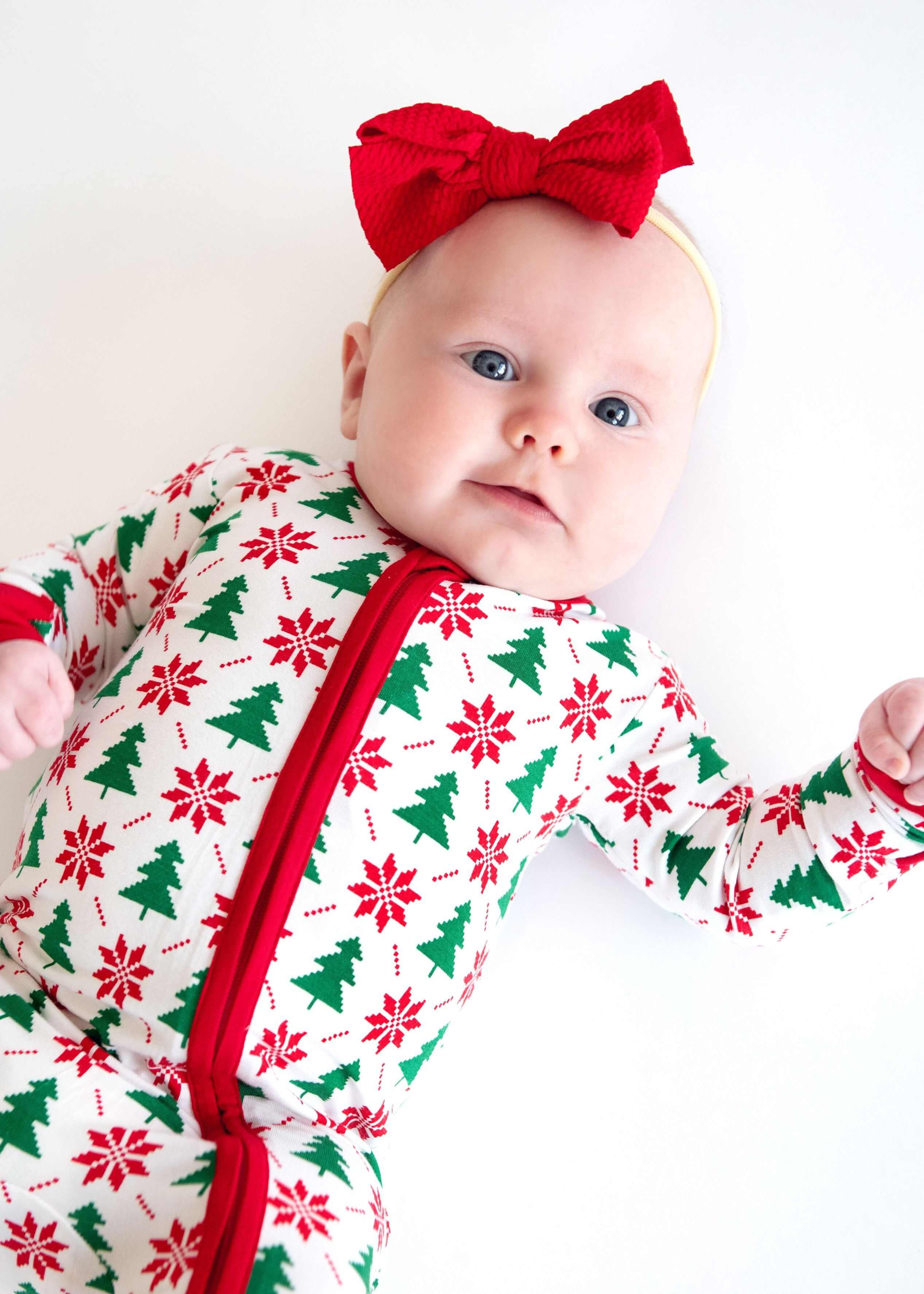 Minky Couture Infant Unisex Zipper Footie worn by a baby with a red bow, featuring festive holiday patterns.