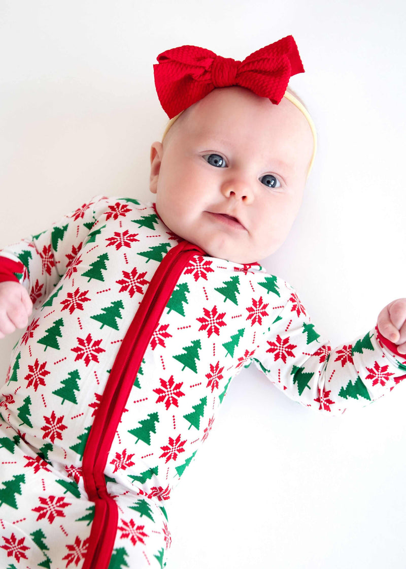 Minky Couture Infant Unisex Zipper Footie worn by a baby with a red bow, featuring festive holiday patterns.