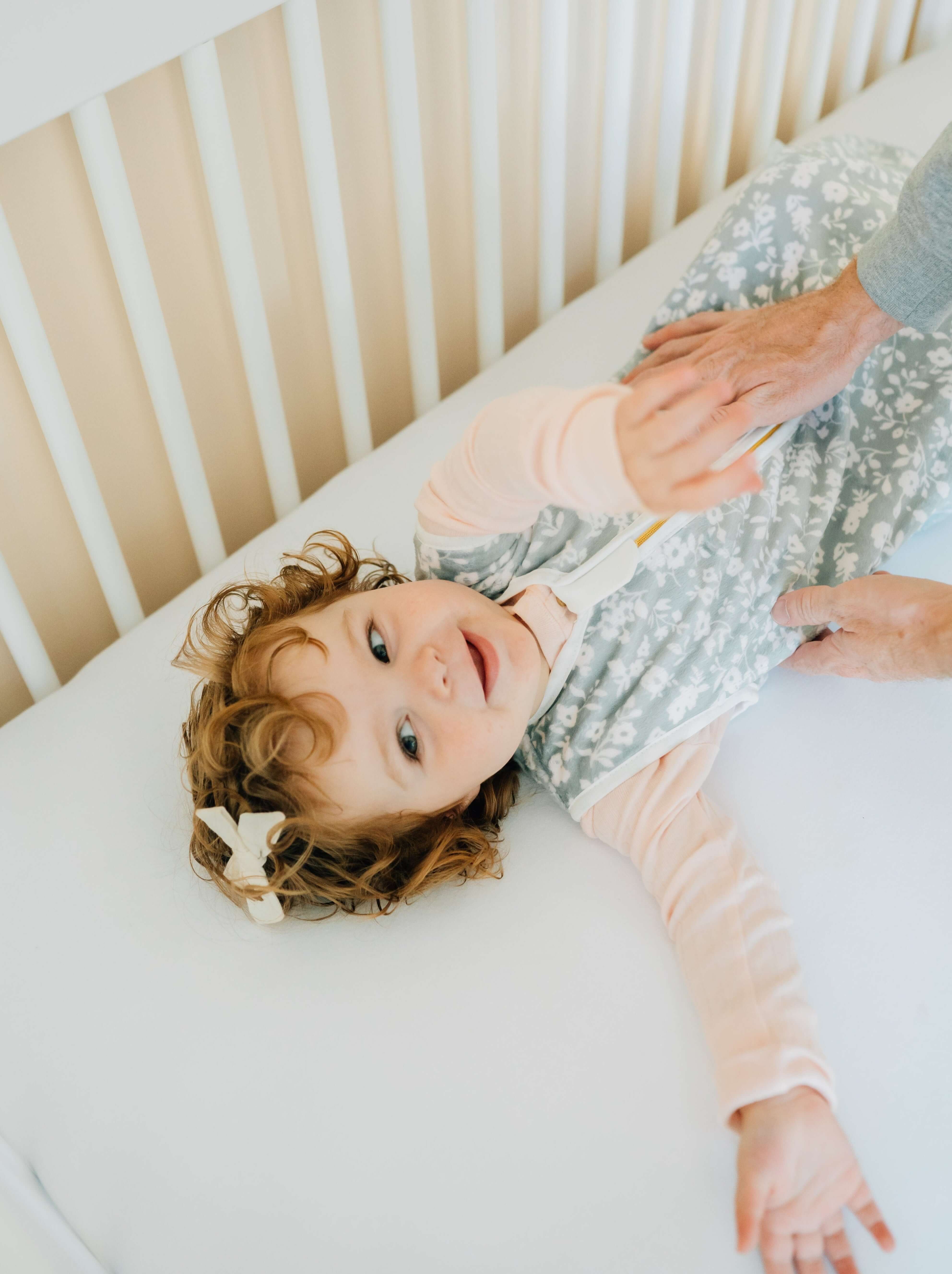 Dainty Floral Sage Wearable Minky Blanket on a smiling baby in a crib, showcasing safe sleep alternative.