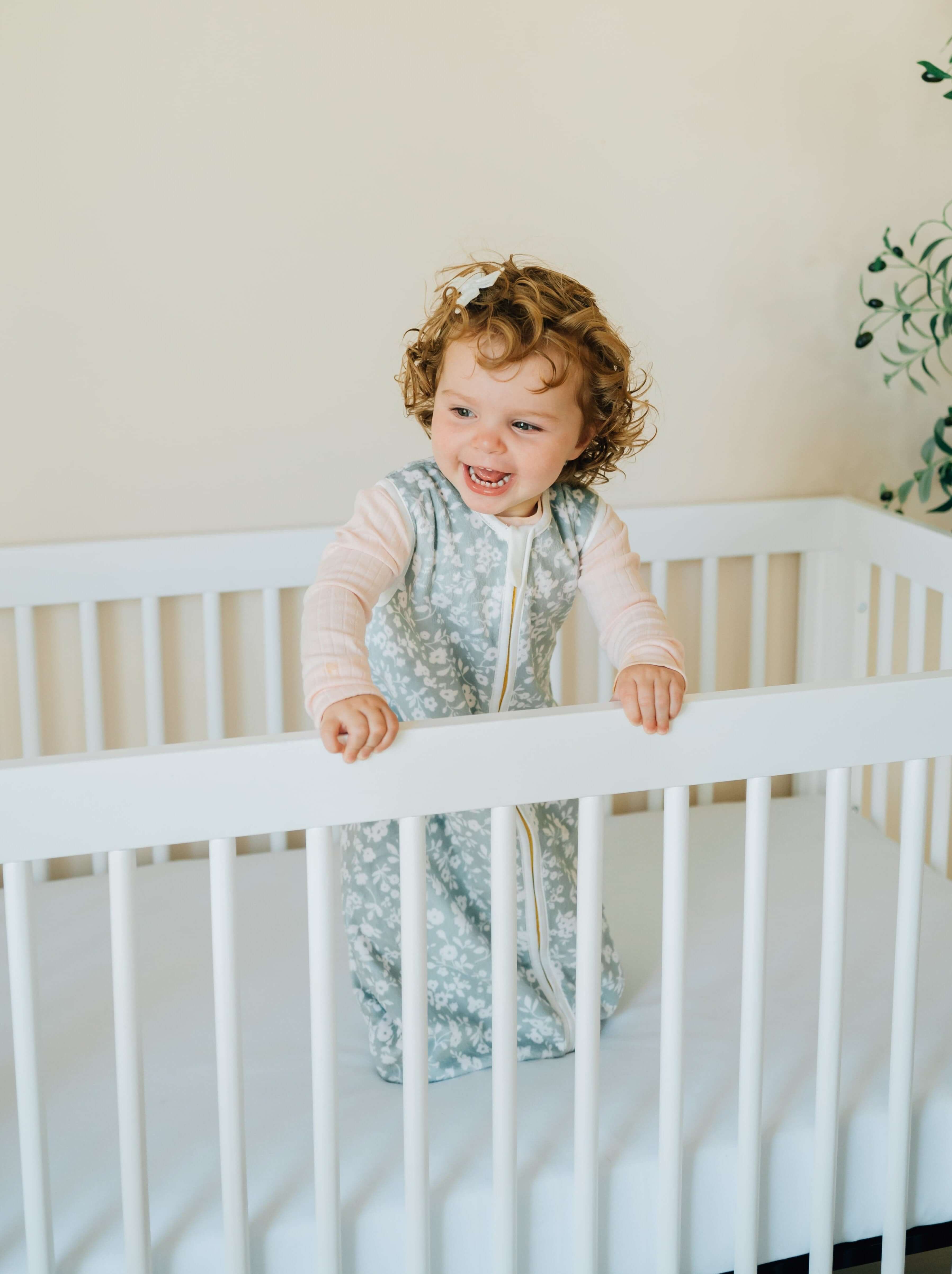 Dainty Floral Sage Wearable Minky Blanket on a happy toddler in a crib, showcasing safe sleep for infants.