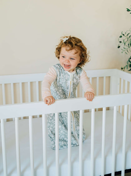 Dainty Floral Sage Wearable Minky Blanket on a happy toddler in a crib, showcasing safe sleep for infants.