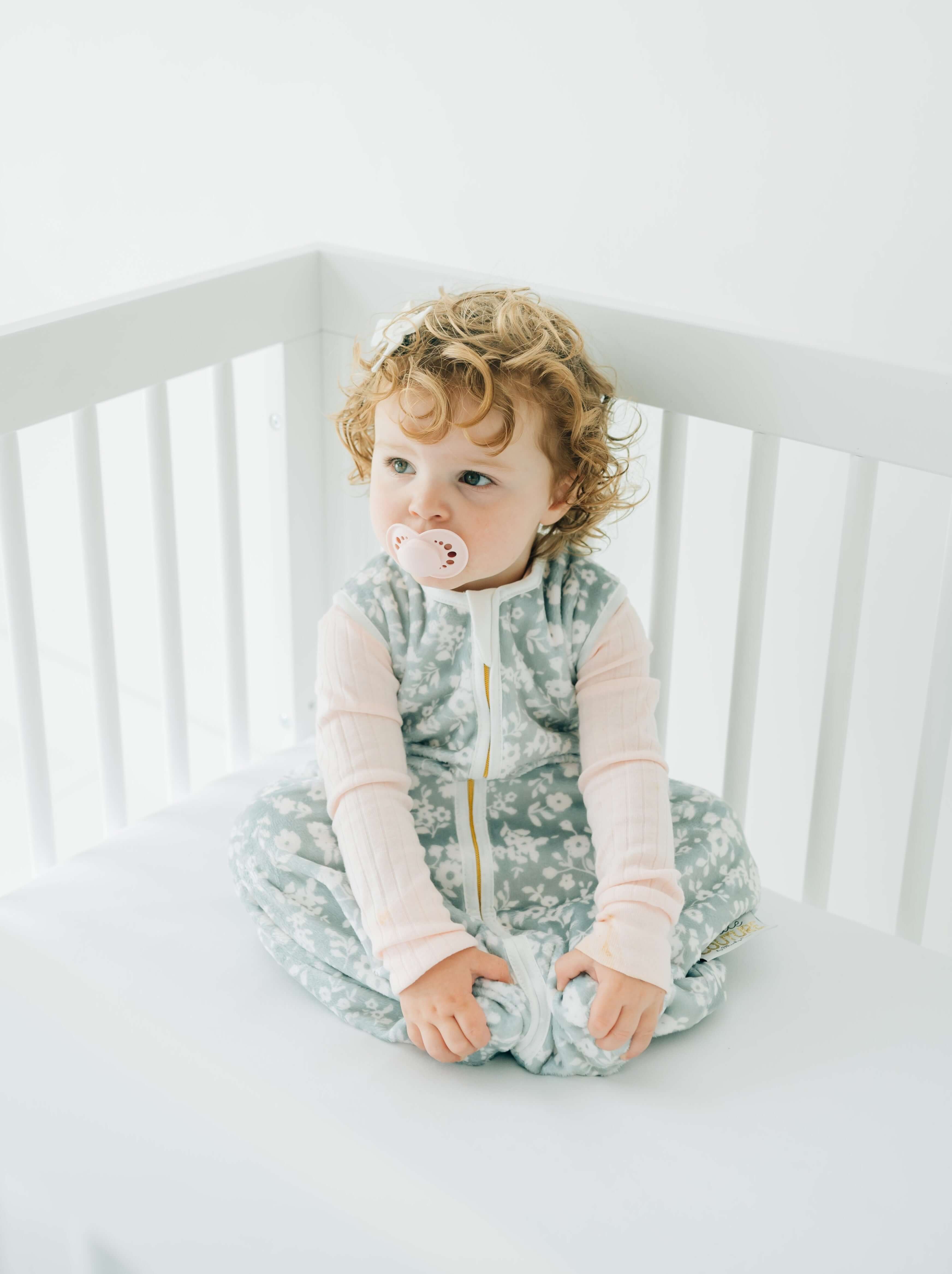 Dainty Floral Sage Wearable Minky Blanket worn by a cute toddler sitting in a crib, cozy and comfortable.