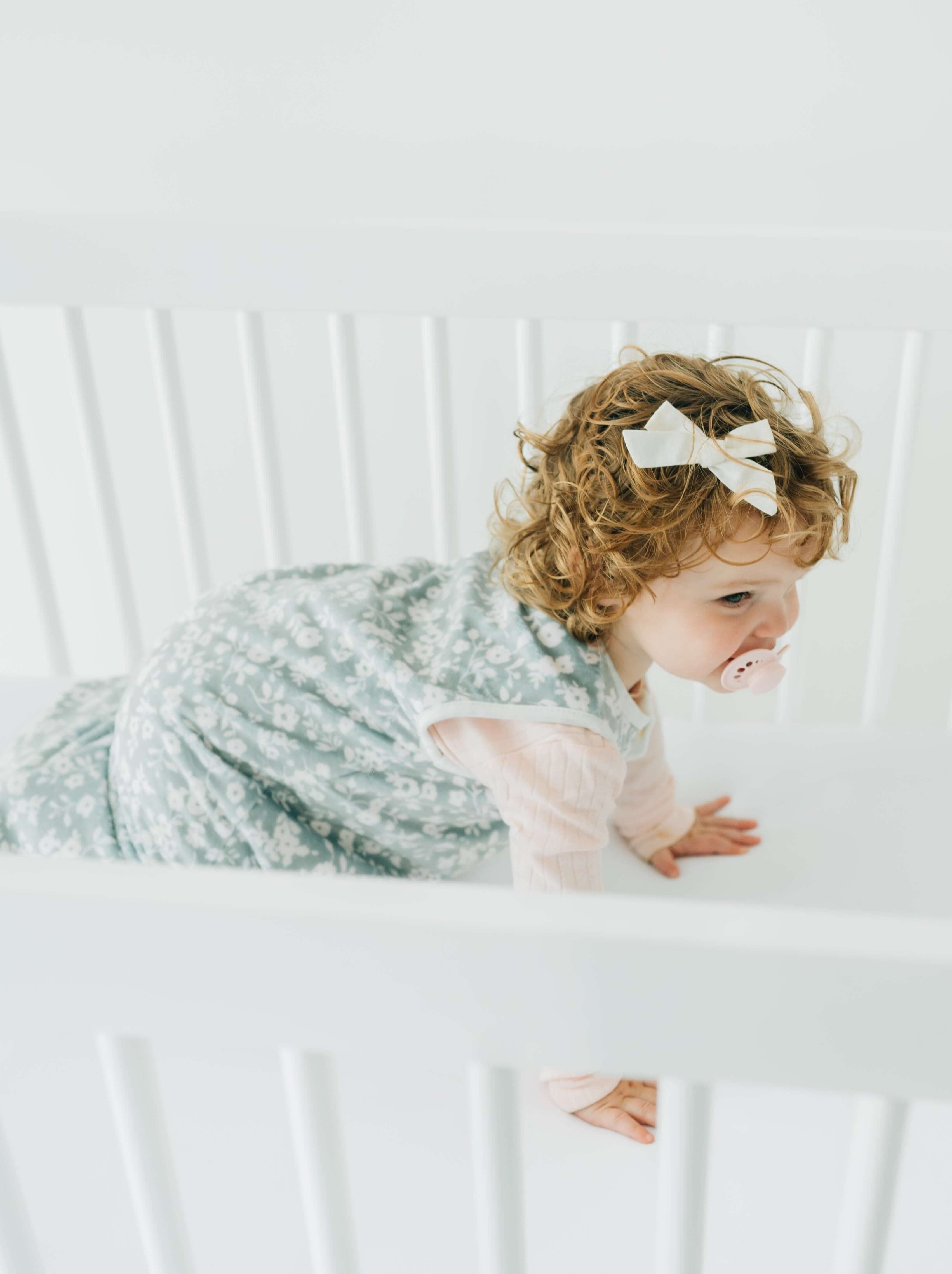 Cute baby in crib wearing Dainty Floral Sage Wearable Minky Blanket, showcasing comfort and safety for infants.