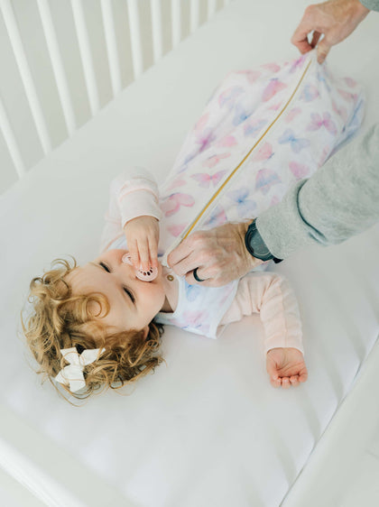 A baby wearing a Butterfly Wearable Minky Blanket, enjoying cozy comfort in a crib.