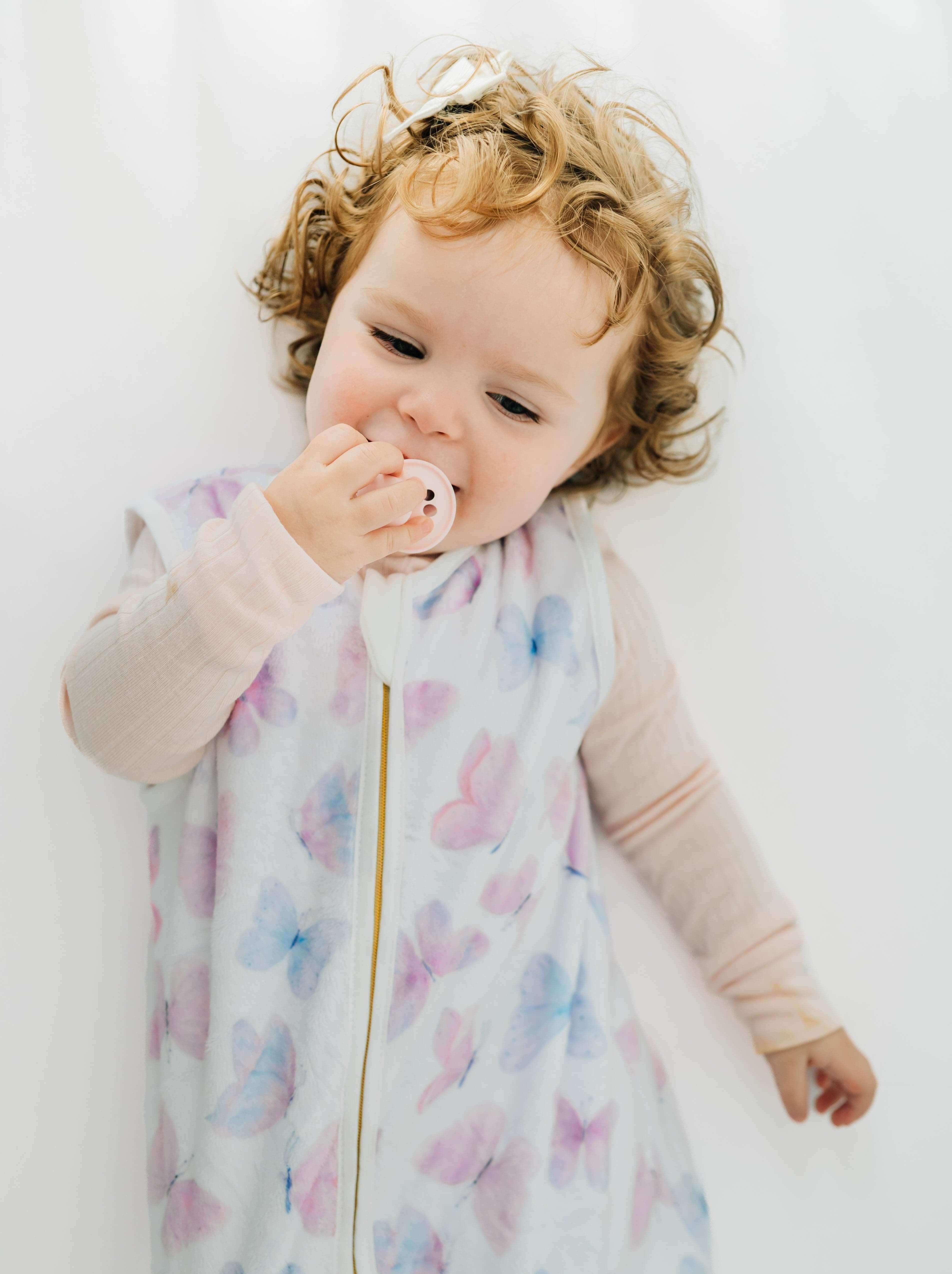 A baby in a Butterfly Wearable Minky Blanket, enjoying comfort while using a pacifier.
