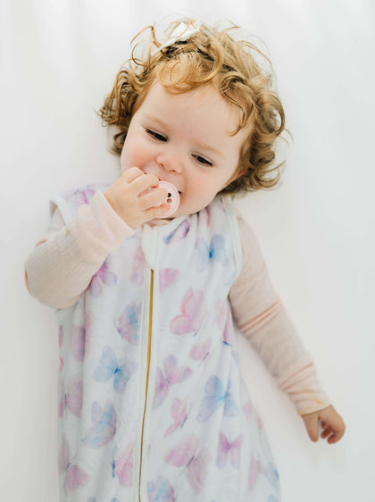 A baby in a Butterfly Wearable Minky Blanket, enjoying comfort while using a pacifier.