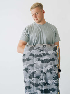 Sleeping Bag Camo held by a young person, showcasing its stylish camouflage design and plush lining.