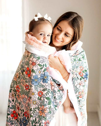 Mom and child wrapped in the Peach Garden Blanket featuring a floral pattern with coral, peach, and blue flowers.