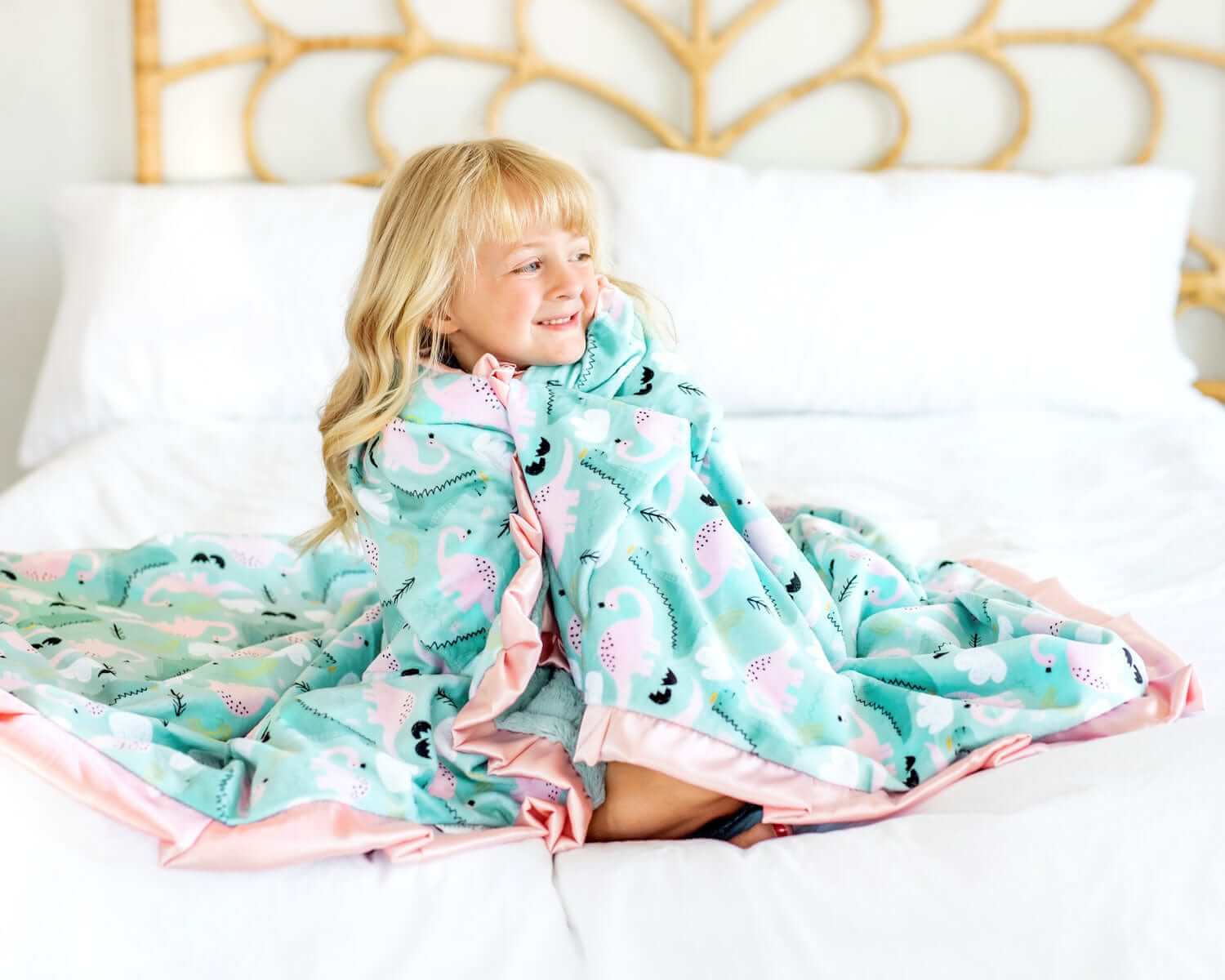 A child wrapped in a Ms. Dino Blanket featuring blue and pink dinosaurs on a light blue background.