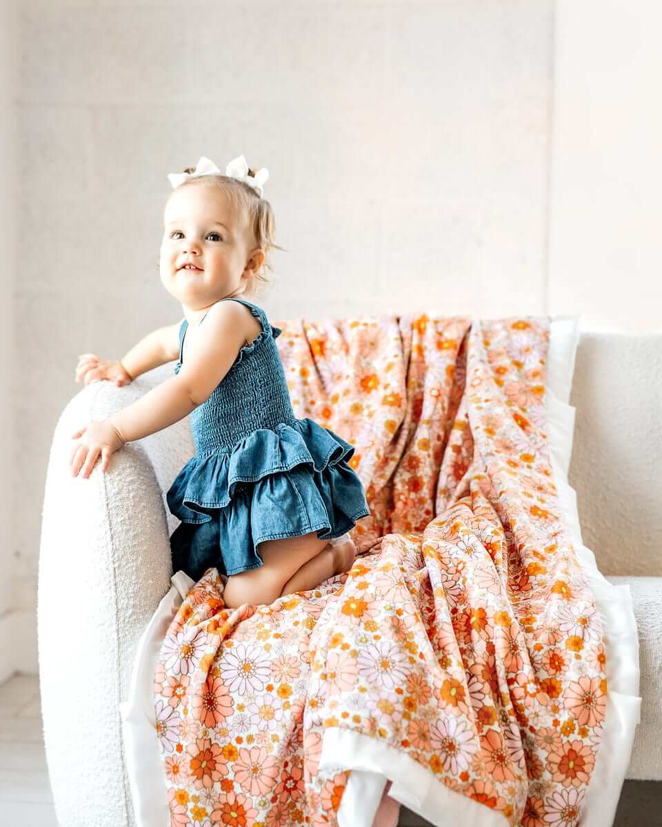 Cute child sitting on a couch with a Boho Floral Blanket draped nearby featuring vibrant flowers in orange, pink, and yellow.