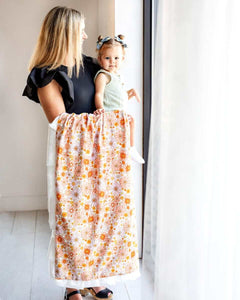 Mom holding her child while draping a Boho Floral Blanket with vibrant flowers by the window.