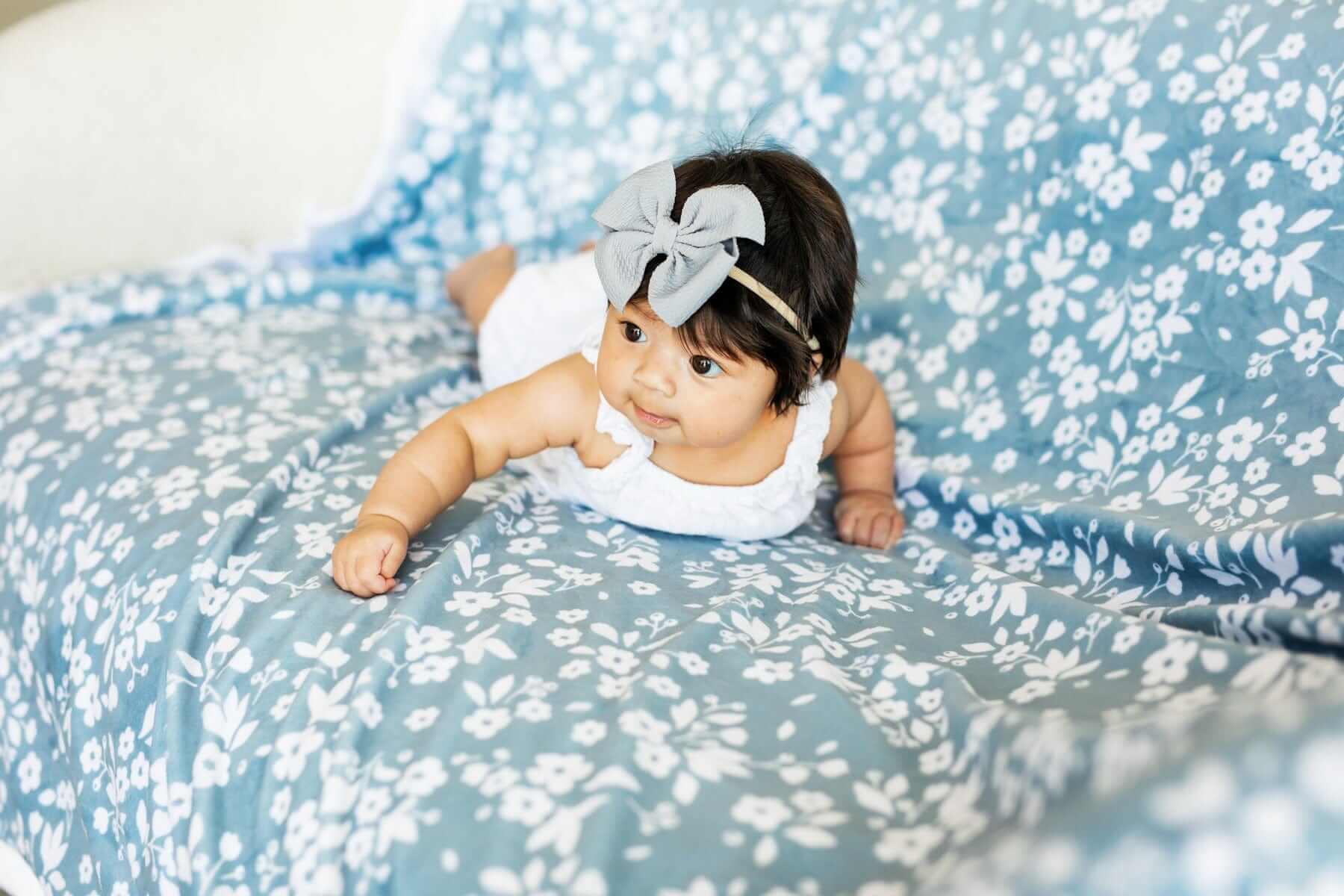 Baby laying on Dainty Floral Blue Blanket with small white flowers and leaves on a light blue background.