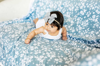 Baby laying on Dainty Floral Blue Blanket with small white flowers and leaves on a light blue background.