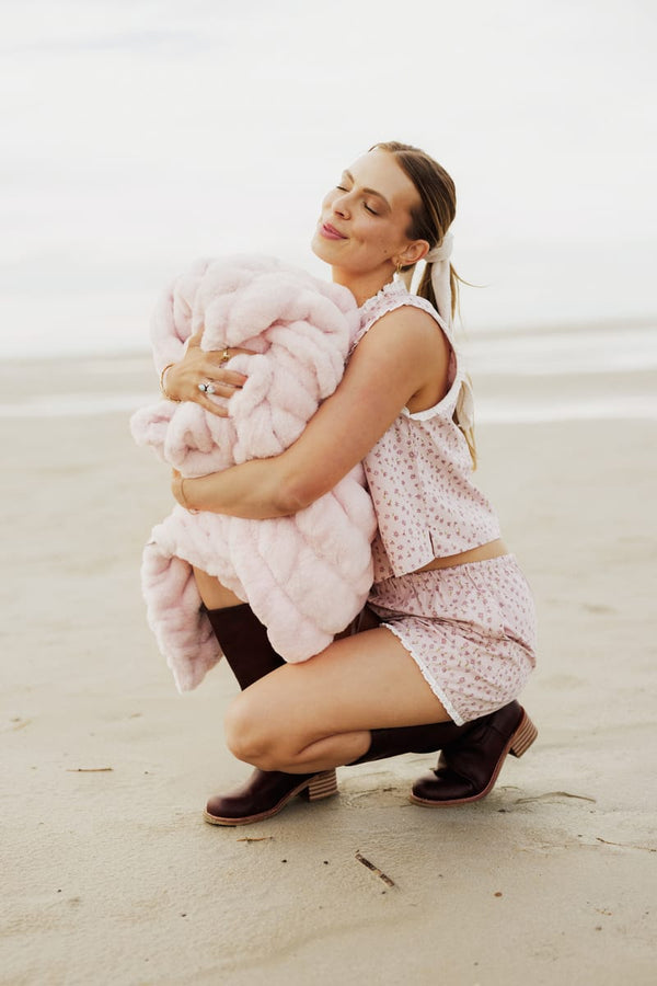 Woman holding a pink fluffy blanket on a beach