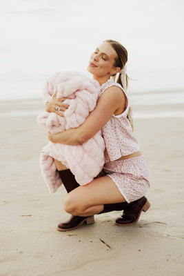 Woman holding a pink fluffy blanket on a beach