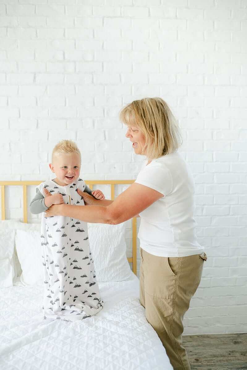 A mom helps a baby wear the Mountains Wearable Minky Blanket, showcasing its comfort and adorable mountain design.