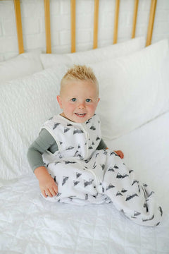 Happy baby wearing the Mountains Wearable Minky Blanket, sitting on a bed surrounded by soft pillows.