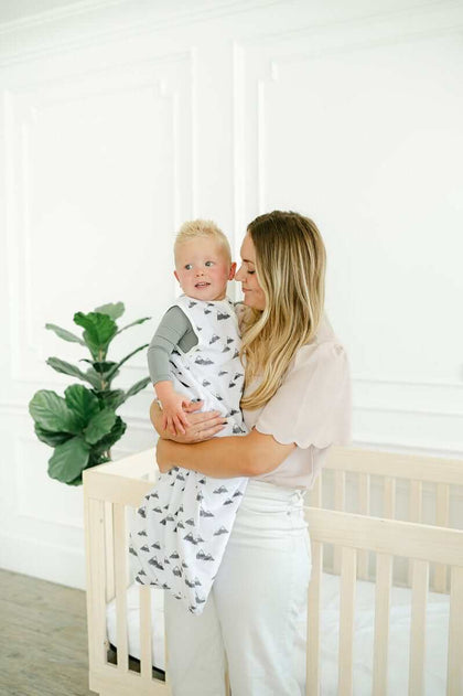 A mother holding her child in a Mountains Wearable Minky Blanket with gray mountains design.