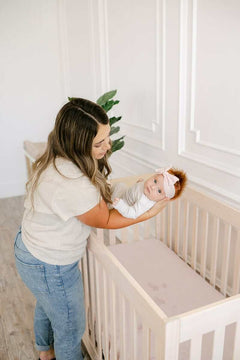 Mom placing her baby in a crib with a cozy Minky Crib Sheet for ultimate comfort.