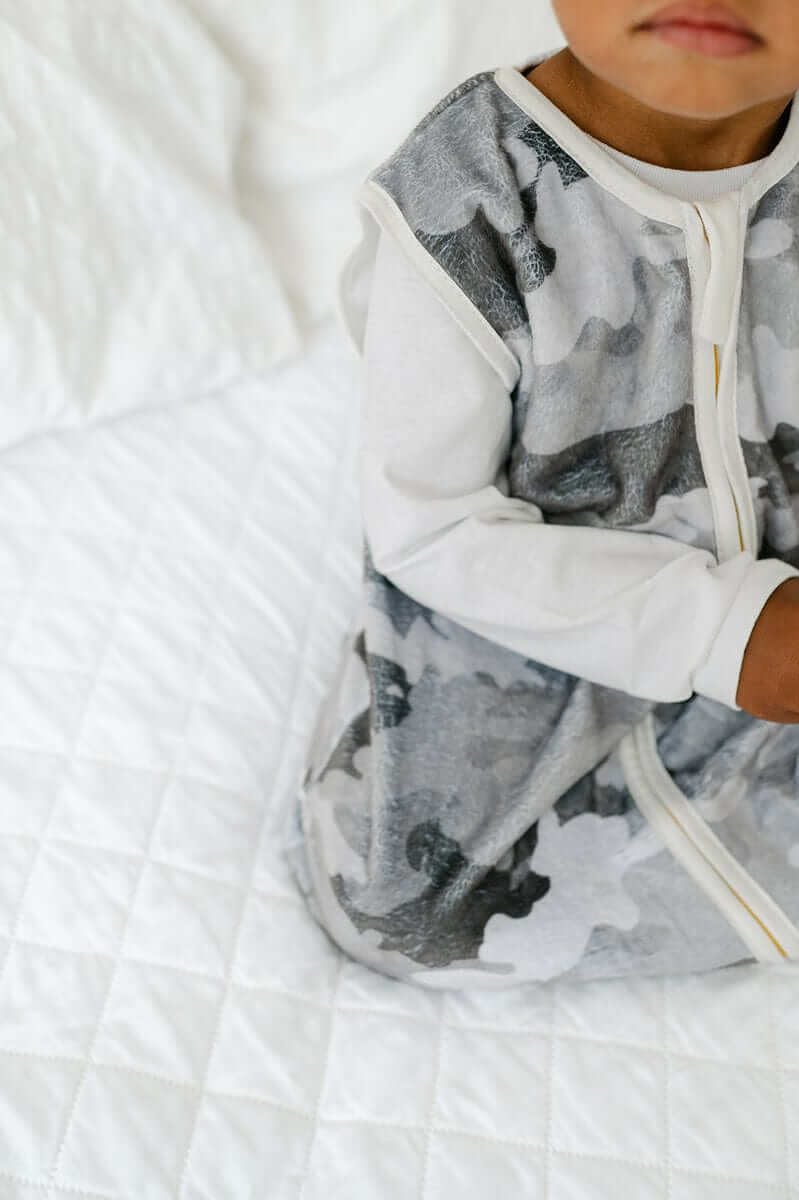 Camo Wearable Minky Blanket in gray camo pattern on a child sitting on a white quilted blanket.