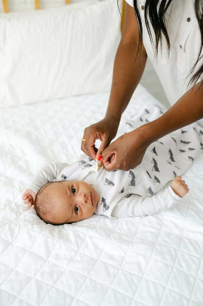 Mountains Wearable Minky Blanket being adjusted on a baby lying on a quilted bed.