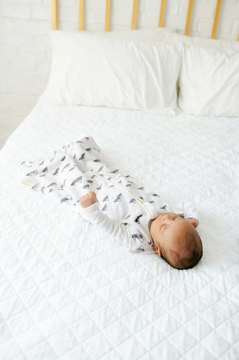 Infant peacefully sleeping in Mountains Wearable Minky Blanket on a cozy white bed.