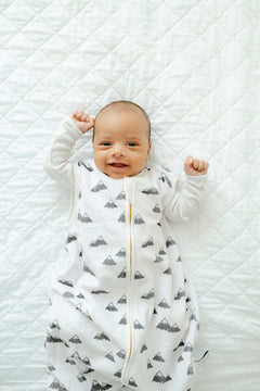 Happy baby wearing Mountains Wearable Minky Blanket with gray mountains and gold zipper on a white quilted background.
