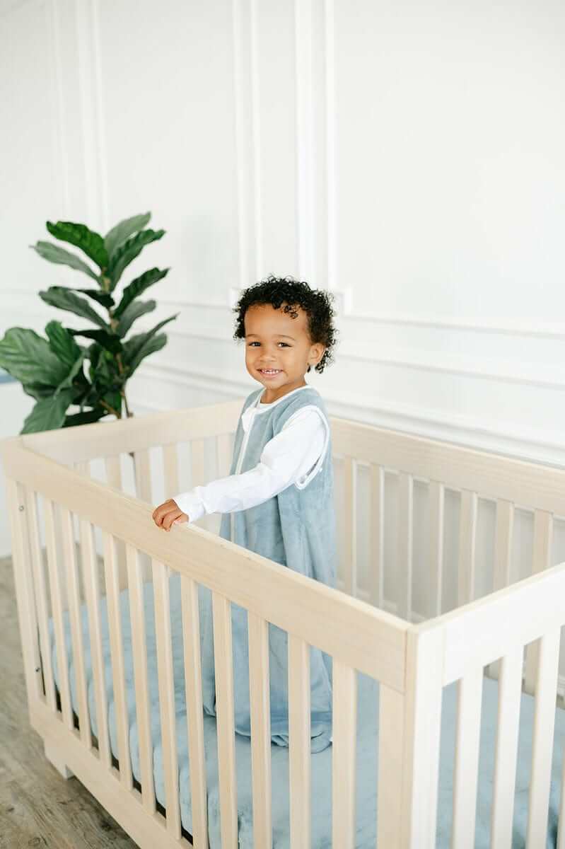 Happy child standing in a crib with a soft Minky Crib Sheet, surrounded by greenery.