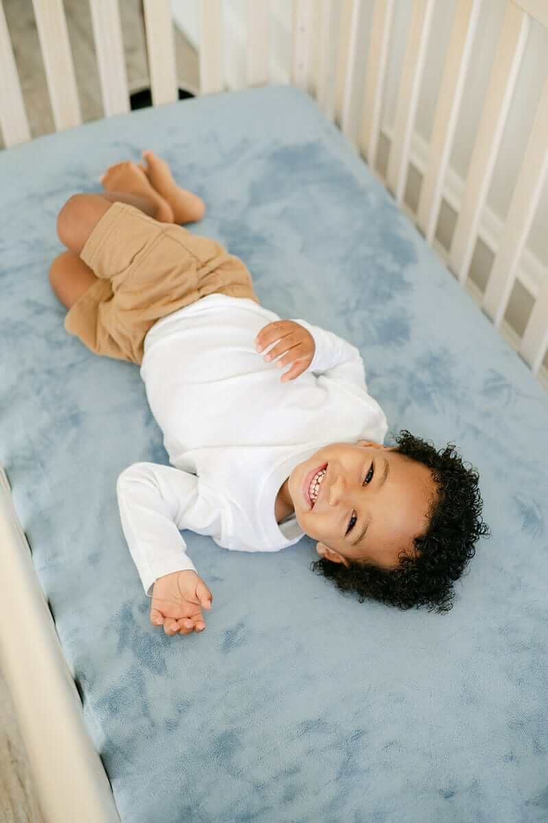 Cozy Crib Sheet with a happy child lying on it, perfect for a restful night's sleep.