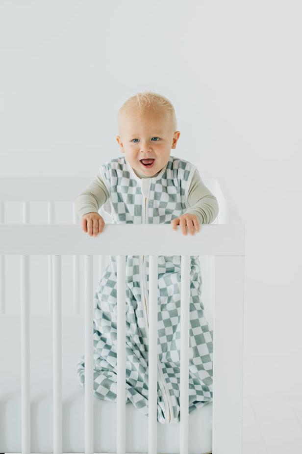 Sage Check Wearable Minky Blanket on a baby in crib, featuring an imperfect check pattern and gold zipper.