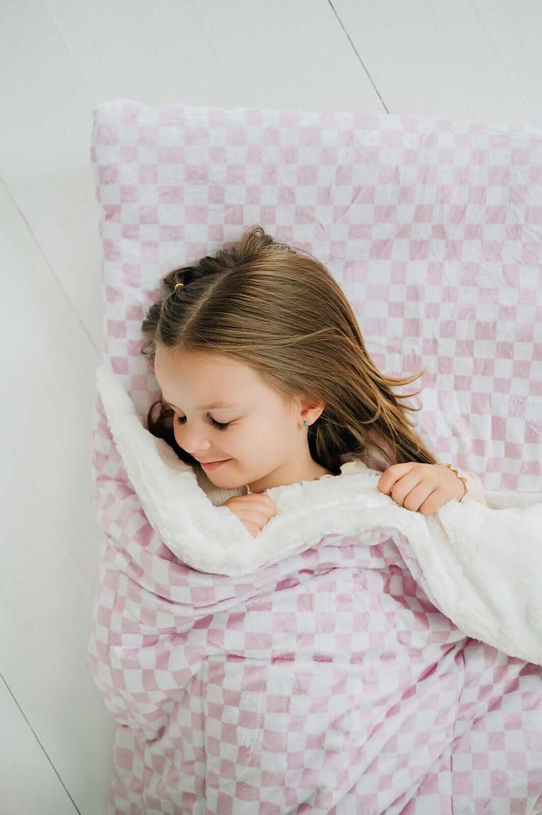 A child peacefully sleeping in a Pink Check Sleeping Bag, showcasing the soft, cozy design and plush lining.