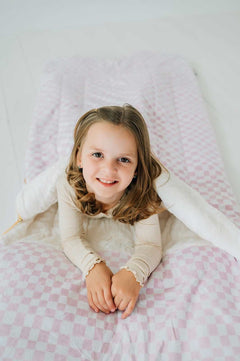 Sleeping Bag in Pink Check, laid out with a smiling girl, showcasing its cozy design and plush material.